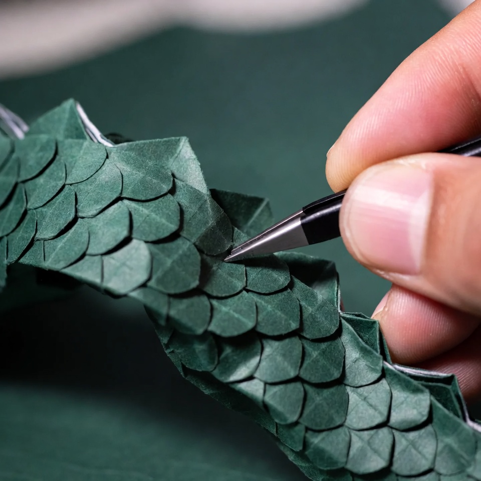 Travail détaillé sur la texture des écailles de dragon en origami à l'aide d'outils.